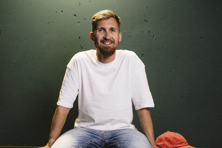 Senior Product Owner sitzt auf einem Regal Senior Product Owner sitzt lässig auf einem dunkelgrünen Regal und lächelt in die Kamera
