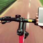 Fahrradfahrer stützt Hand auf Lenker, um Smartphone zu bedienen.