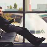 Ein Mann mit Bügel-Kopfhörern sitzt am Terminal auf den Sitzen und schaut aufs Smartphone