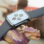 Eine Apple Watch mit schwarzem Armband ruht dekorativ auf zwei Spielzeug-Dinosaurieren. Auf dem Display ist die Uhrzeit zu lesen.