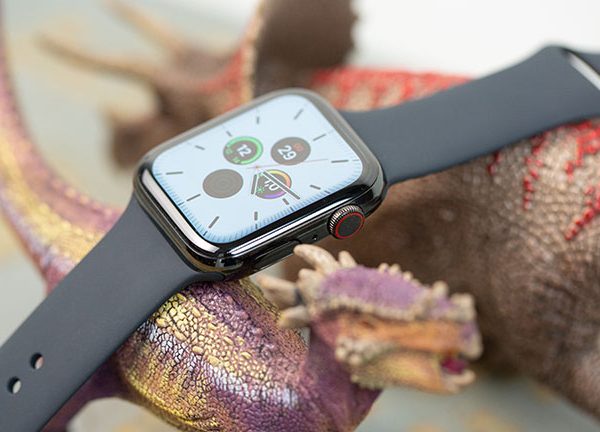 Eine Apple Watch mit schwarzem Armband ruht dekorativ auf zwei Spielzeug-Dinosaurieren. Auf dem Display ist die Uhrzeit zu lesen.