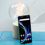 Das OnePlus 8 Pro steht aufrecht angelehnt an eine Glühbirne. Das Display ist aktiviert und zeigt den Home-Bildschirm.