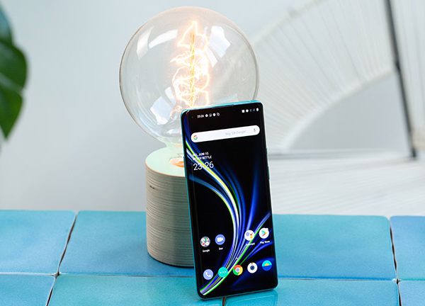 Das OnePlus 8 Pro steht aufrecht angelehnt an eine Glühbirne. Das Display ist aktiviert und zeigt den Home-Bildschirm.