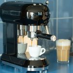 Eine Espressomaschine im Retro-Look der Marke Smeg steht auf einer Küchenzeile und bereitet einen Espresso zu.