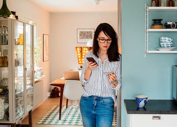 Eine Person steht an eine Wand gelehnt und hält ihr Smartphone in der Hand.