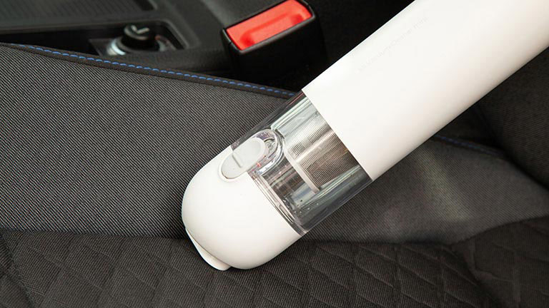 Der Xiaomi Mi Vacuum Cleaner Mini saugt entlang der Längsnaht auf der Sitzfläche eines Autositzes.