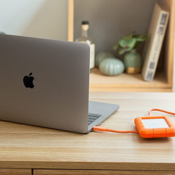 Ein aufgeklapptes MacBook steht auf einem Schreibtisch. Daneben liegt eine angeschlossene, externe Festplatte.