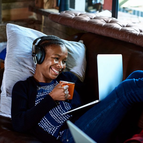 Eine Person liegt auf einem Sofa, hält eine Tasse in der Hand und videotelefoniert über ein Notebook.