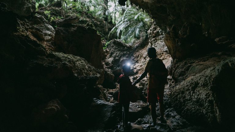 Zwei Kinder stehen in einer Felsgrotte, das kleinere von Ihnen trägt eine Stirnlampe am Kopf.