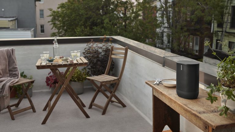 Auf einem Balkon steht ein Bluetooth-Lautsprecher auf einem Tisch, im Hintergrund ein kleiner gedeckter Tisch für Zwei.