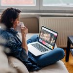 Eine Person sitzt mit einer Tasse in der Hand auf dem Sofa und schaut auf ihrem Laptop auf das Hauptmenü von TVNOW.