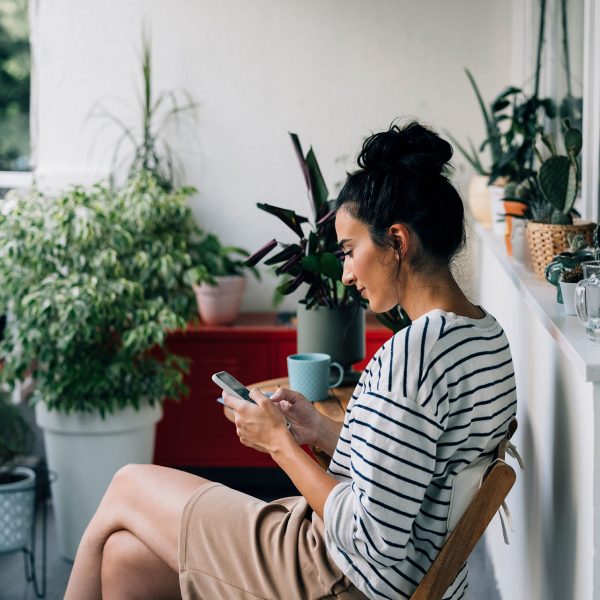 Eine Person sitzt auf einem Balkon und hält ein Smartphone in der Hand.