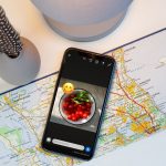 Ein iPhone liegt auf einer Landkarte. Auf dem Bildschirm ist das Foto einer Speise zu sehen, das über WhatsApp als Story geteilt werden soll.