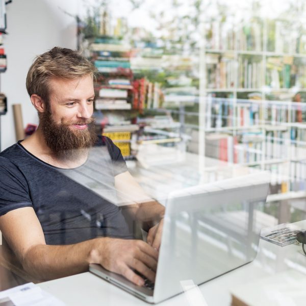 Eine Person sitzt an einem Laptop und tippt. Im Hintergrund sind Bücherregale zu sehen.