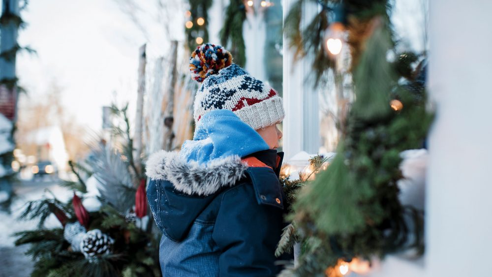 Ein Kind schaut durch ein Fenster in ein weihnachtlich geschmücktes Gebäude.