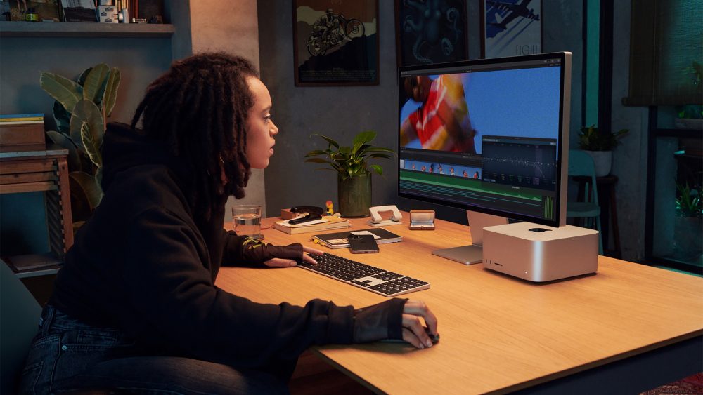 Eine Person sitzt an einem Schreibtisch, auf dem ein Mac Studio und das Studio Display stehen.