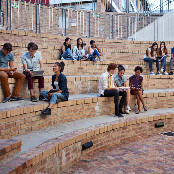 Mehrere Studierende sitzen auf ihrem Campus in Gruppen zusammen.