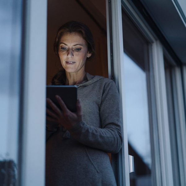 Eine Person steht mit einem Tablet in der Tür zur Terrasse.