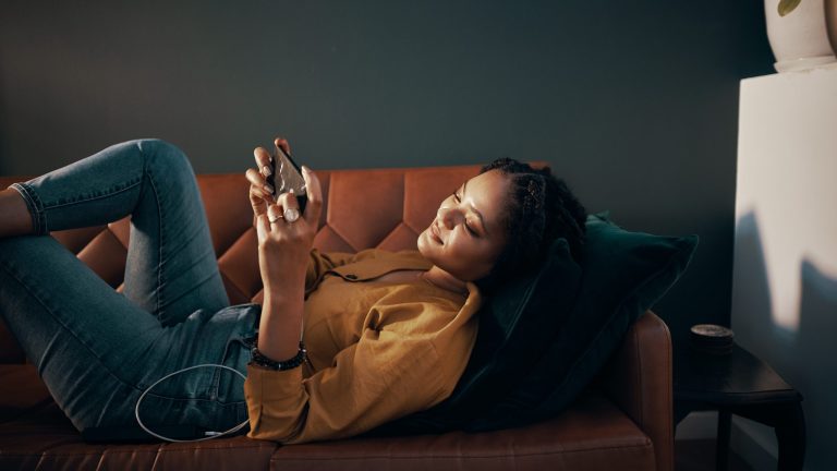 Eine Person liegt auf einem Sofa und spielt dabei auf ihrem Smartphone.