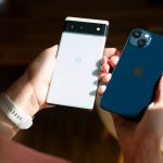 Zwei Hände halten jeweils ein Smartphone: Einmal ein weißes Google Phone und einmal ein dunkelblaues iPhone.