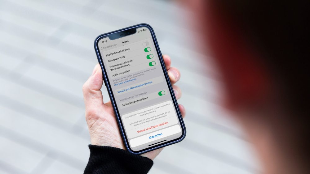 Eine Person hält ein iPhone in den Händen. Darauf sind die Einstellungen zu sehen, in denen sich der Browser-Cache leeren lässt.