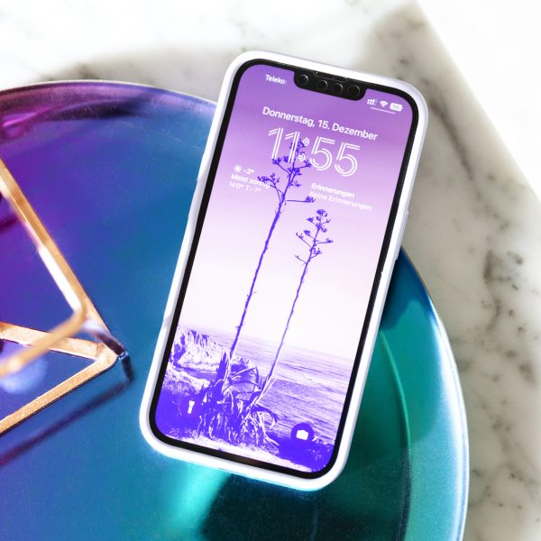 Ein iPhone liegt mit eingeschaltetem Bildschirm in einer Schale. Auf dem Gerät ist ein lilafarbenes Hintergrundbild zu erkennen.