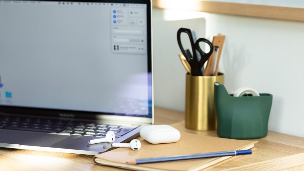 Neben einem MacBook Pro liegen AirPods und das dazugehörige Case.