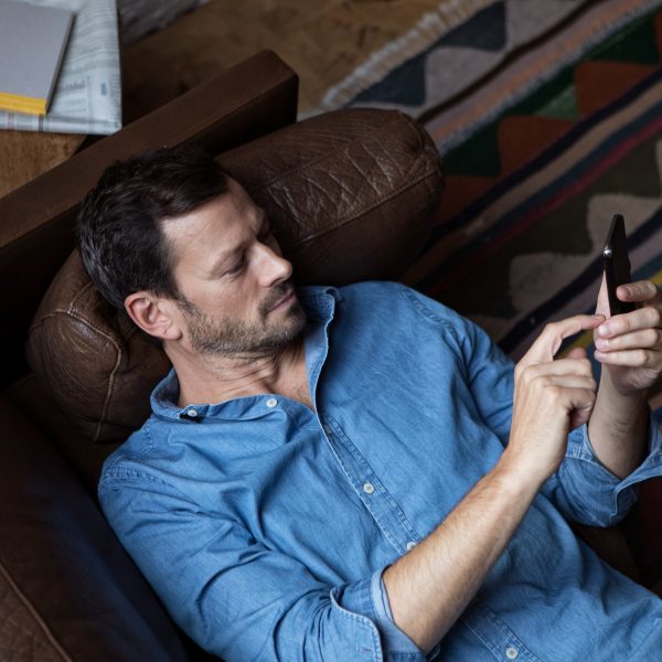 Eine Person liegt auf einem Sofa und bedient ihr Smartphone.