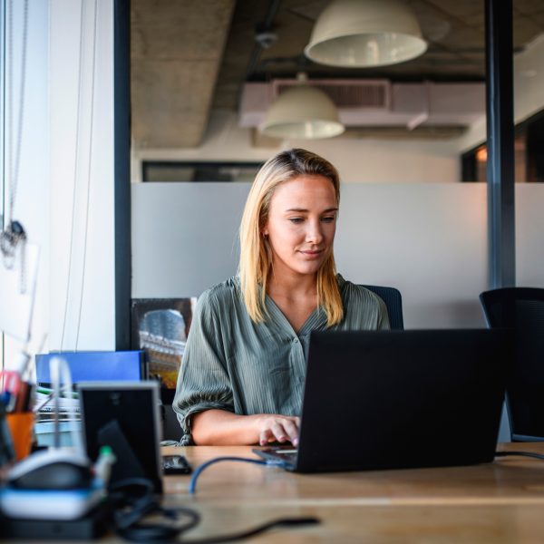 Eine Person sitzt in einem Büro vor einem Windows-Laptop.