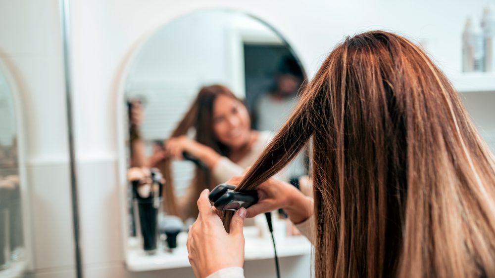 Eine Person steht vor einem Spiegel und glättet sich eine Haarsträhne.