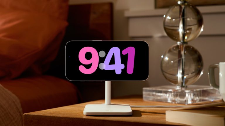 Ein iPhone 14 Pro hängt im Querformat auf einer Ladestation auf einem Nachttisch und zeigt die Uhrzeit an.