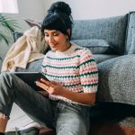 Eine Person sitzt vor einem Sofa auf dem Boden und hält ein iPhone in der Hand.