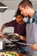 Zwei Personen stehen zusammen an einem Herd und kochen etwas.