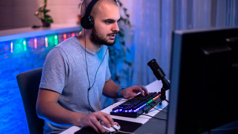 Eine Person mit einem Kopfhörer auf dem Kopf sitzt vor einem Gaming-PC und spielt etwas.