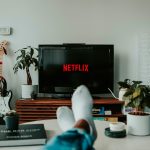 Eine Person hat die Füße auf den Tisch gelegt und schaut auf dem TV Netflix.