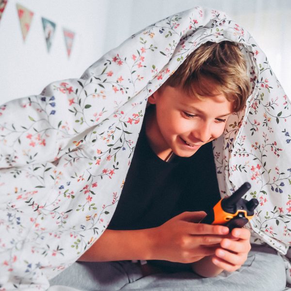 Ein Kind unter einer Bettdecke hält ein Walkie-Talkie in der Hand.