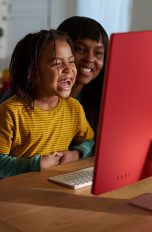 Zwei Kinder und eine erwachsene Person sitzen vor einem iMac.