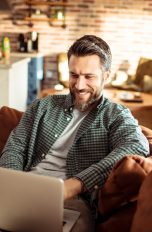 Eine Person sitzt auf einem Sofa und grinst in einen Laptop.