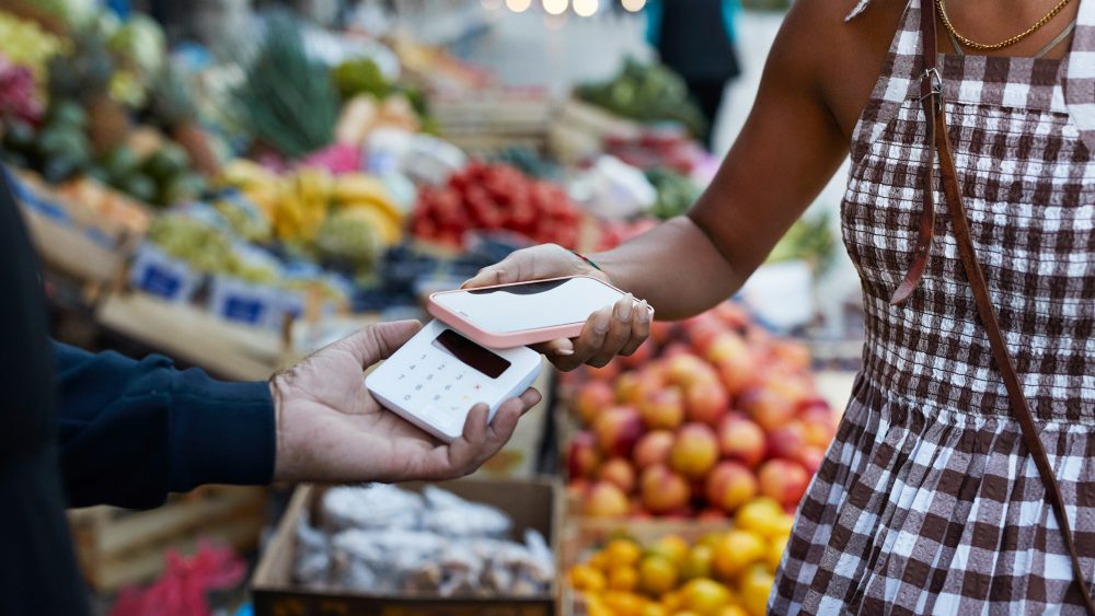 Eine Person hält ihr iPhone an ein Kartenlesegerät um etwas per Apple Pay zu bezahlen.