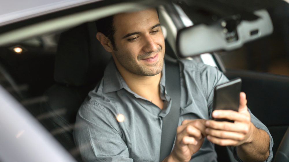 Eine Person sitzt im geparkten Auto und bedient ein Smartphone.