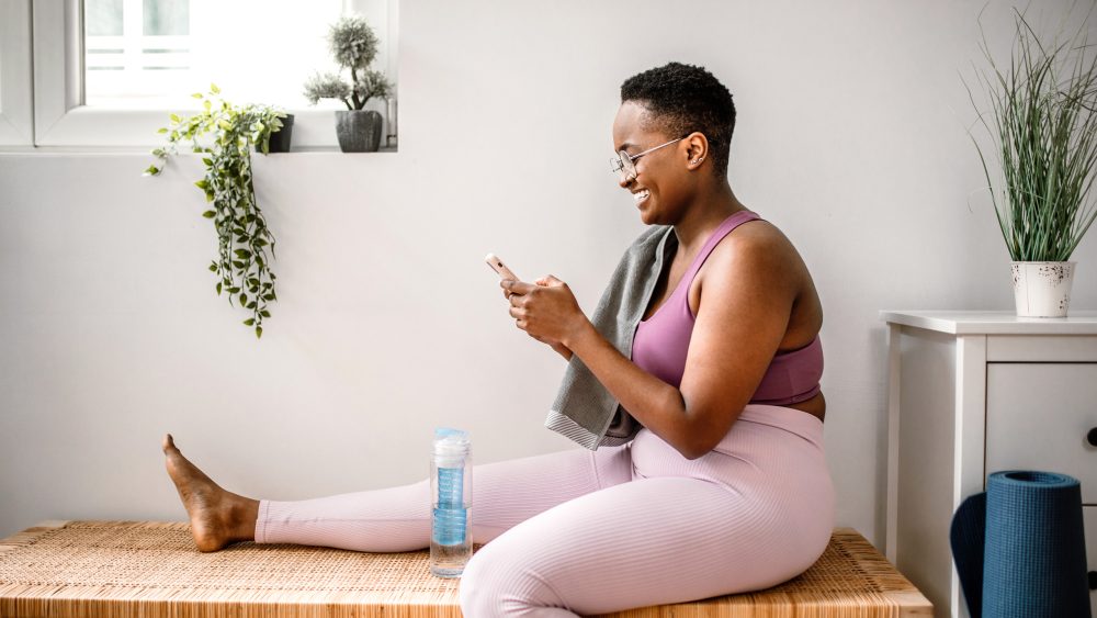 Eine Person sitzt in Sportoutfit zu Hause und scrollt auf ihrem Smartphone.