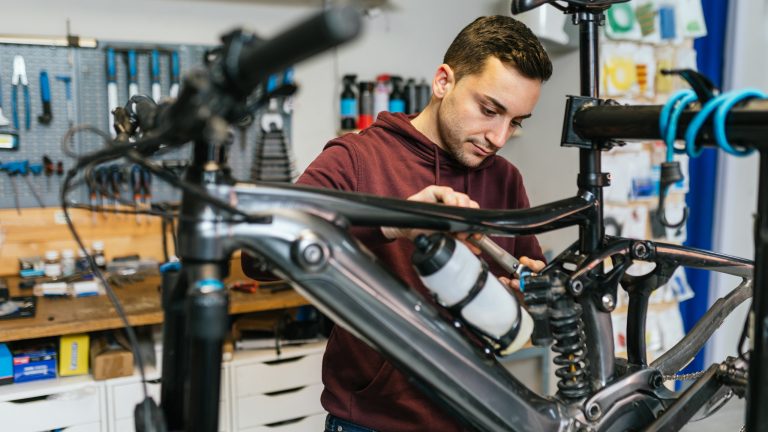 Eine Person schaut in einer Werkstatt an der Federung eines E-Bikes.
