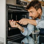 Eine Person in einem Blaumann schraubt an einem Elektroherd.