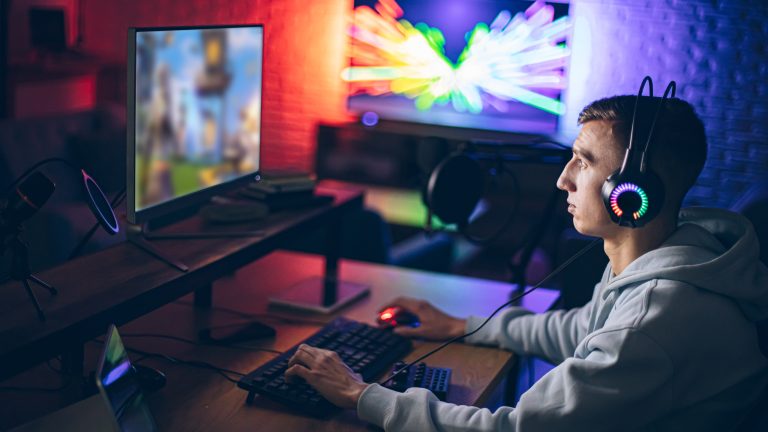 Eine Person sitzt vor einem Gaming Set-up mit bunten LED-Lichtern im Hintergrund.