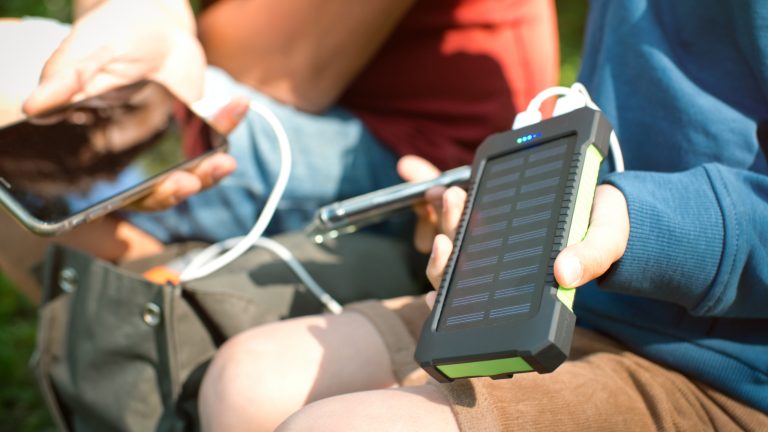 Zwei Personen sitzen im Grünen und haben ihre zwei Smartphones an eine kleine Solar-Powerbank angeschlossen.