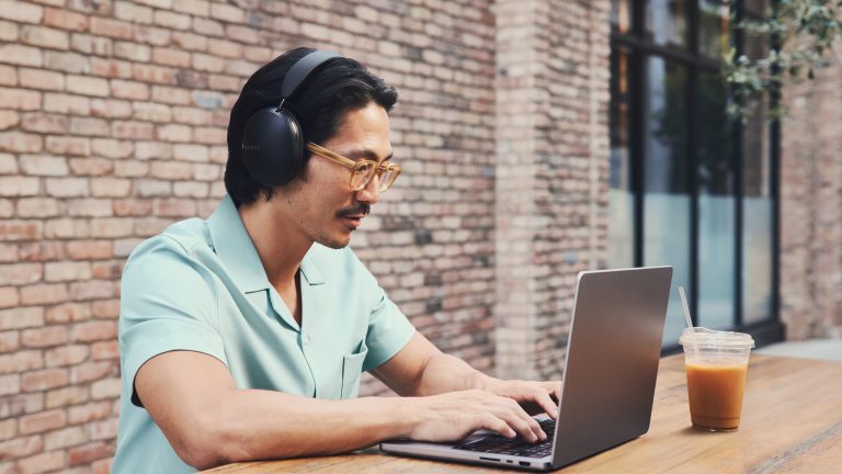 Eine Person sitzt an einem MacBook Pro und trägt dabei Sonos Ace in Schwarz.