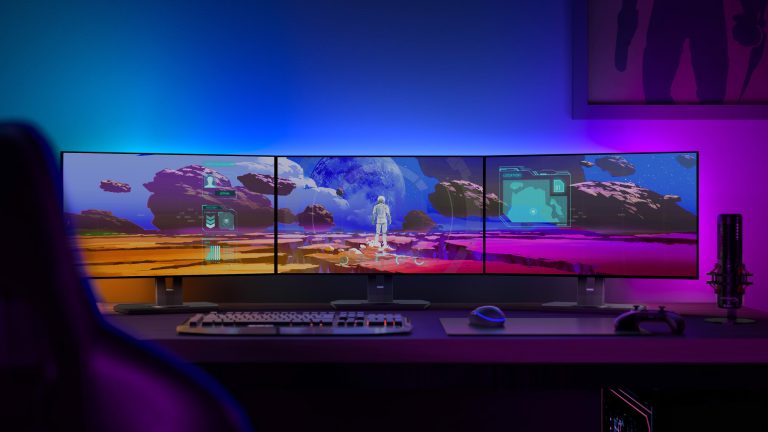 Blick auf ein Gaming-Setup mit indirekter, bunter Beleuchtung hinter drei Monitoren.