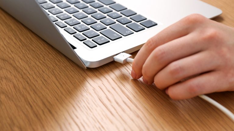 Eine Person steckt ein Ladekabel in ein Macbook.