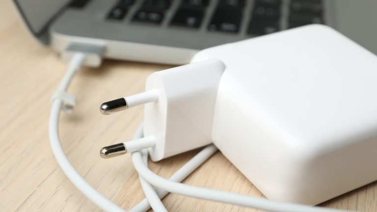 Ein Apple-Netzteil und Ladekabel liegen neben einem Macbook.