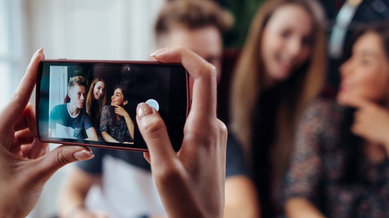 Eine Person macht mit dem Smartphone ein Foto von drei anderen Personen.